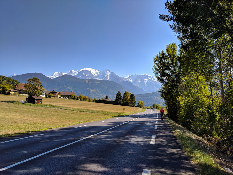 A cyclist on the road with the snow capped mountains of the French Alps in the bacground.