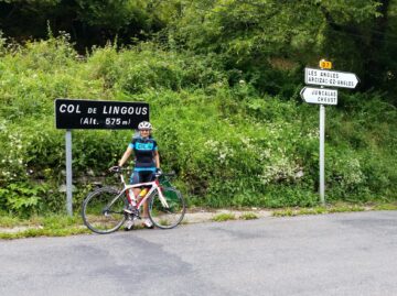 Female cyclist standing at the summit sign of the Col de Lingous in the French Pyrenees
