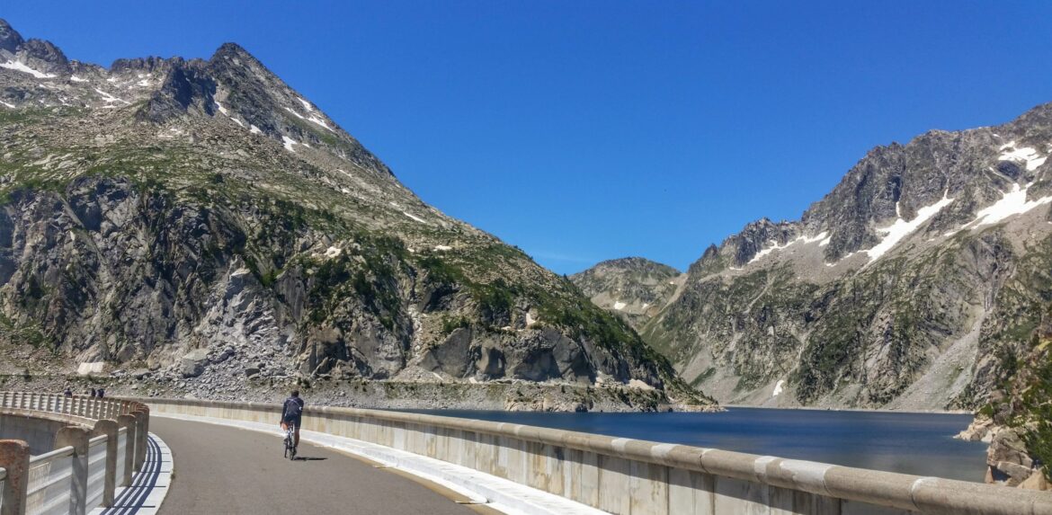Cyclist riding across the dam wall at the top of Lac de Cap de Long. A lesser known climb in the French Pyrenees